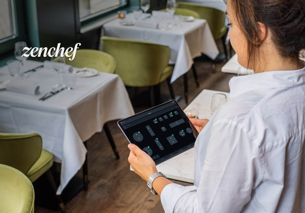 Eine Restaurantmitarbeiterin schaut auf ihr Tablet und sieht die Tischverwaltung. Oben links im Bild ist das Logo von Zenchef sichtbar.