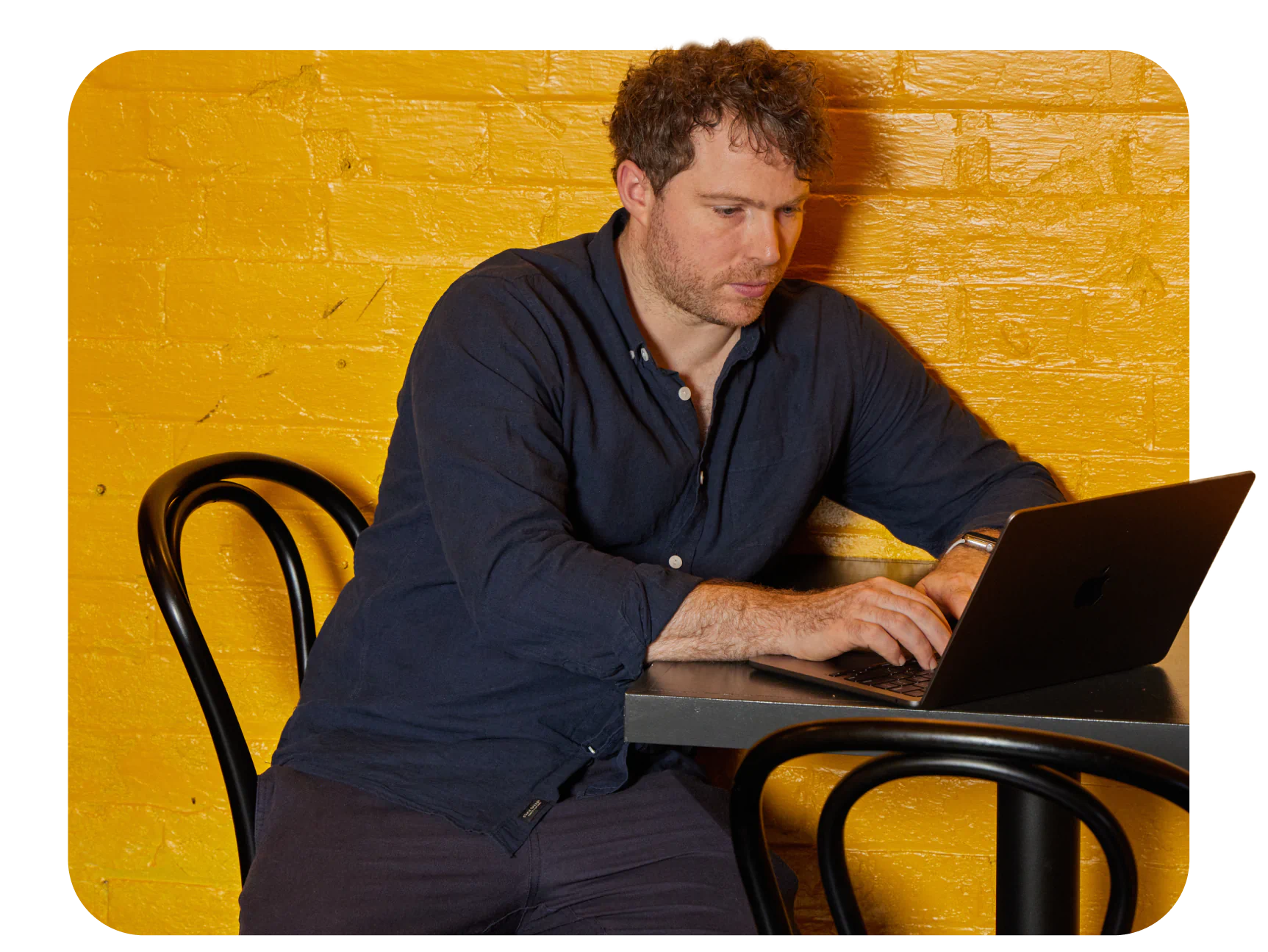 Eine Person sitzt an einem Tisch und arbeitet an einem Laptop.